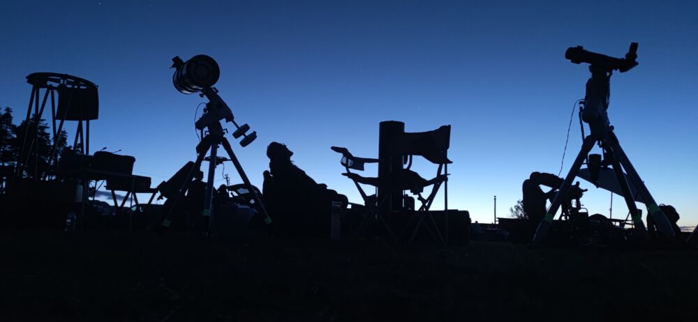 Instruments d'observation en ombres chinoises sous un ciel de crépuscule sans nuages. Un observateur assis dans un fauteuil pliant scrute le ciel en rêvant.
